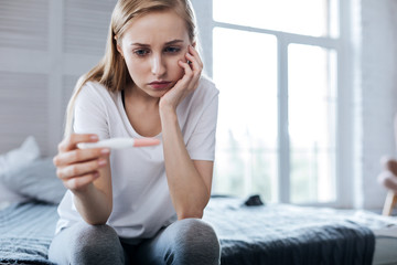Sadness. Upset pretty woman sitting and holding her pregnancy test