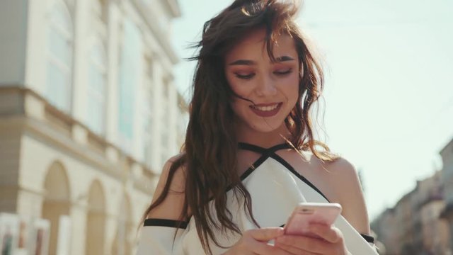 Close up view of happy young brunette woman walking and surfing the internet via smartphone. Modern communication, insta blogger, being online, social networks. Female portrait