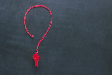 Sports whistle on a red lace. It is laid out in the form of a question mark. Concept- sport...