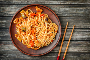 Udon stir-fry noodles with chicken, sweet and sour sauce and food sticks on wooden table