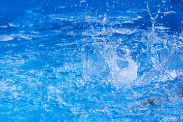 Splashes of clear blue fresh water in pool, air bubbles, water drops, sea wave on blue background with sunny reflections.