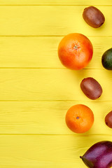 Border from colorful fruits and copy space. Mix of tropical fruits on yellow wooden background and text space, vertical image.