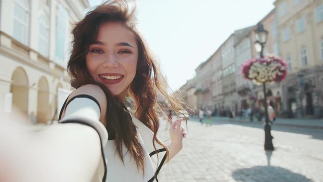 Cute smiling woman poses to camera, acts cheerfully, shows peace sign in the central square. Cuteness, vlogging, social networks. Talking selfie. Female portrait