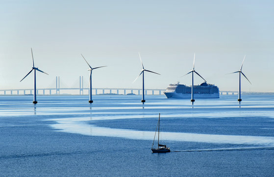 Very large passenger ship and a small sailboat pass offshore wind turbines near the Oresund Bridge between Denmark and Sweden 