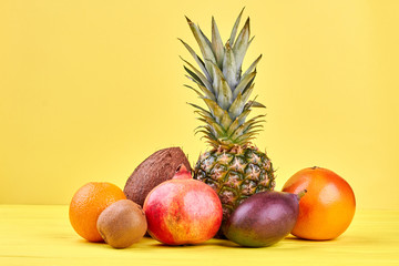 Composition with tropical fruits on yellow background. Fresh pineapple, coconut, pomegranate, grapefruit, kiwi fruit, orange and mango on colorful background.