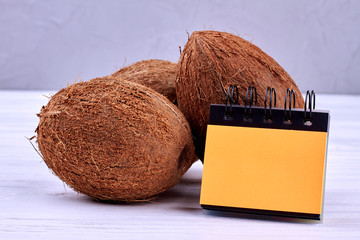 Set of coconuts and blank paper notepad. Fresh brown coconuts and binder notebook on wooden...