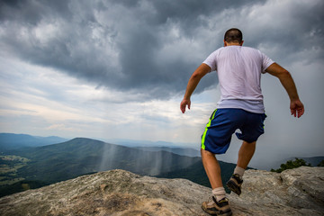 Man Running Towards the edge of  McAfee Knob edge above scenic stormy Valley.