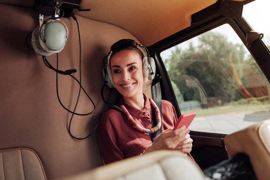 Always work. Satisfied enthusiastic woman sitting in helicopter and holding phone