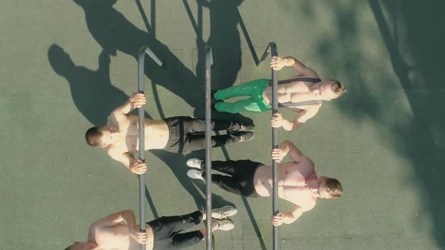 Young athletes are making pull-ups on the parallel bars at a workout in the open air