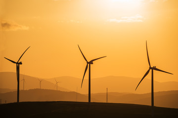 Wind power generator on a hill  at sunset, silhouettes of mountain peaks.
