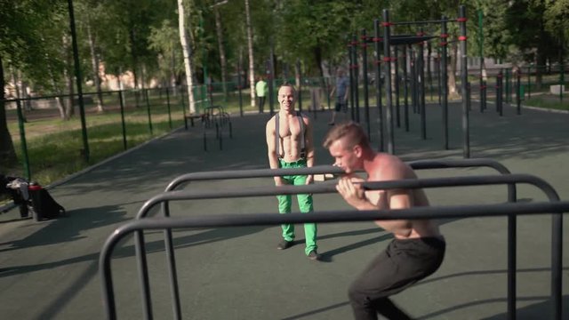 Cheerful young athletes at a workout on the parallel bars in the open air