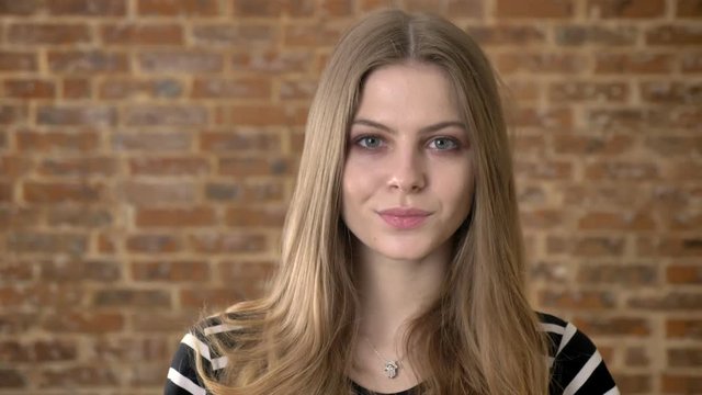Young confident blonda is watching at camera, brick background
