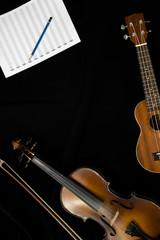 Top view of violin and ukulele with musical note sheet on the black background