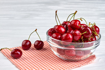Ripe delicious cherries in glass bowl. Fresh juicy berries on cloth vintage napkin on white background. Tasty seasonal fruit.