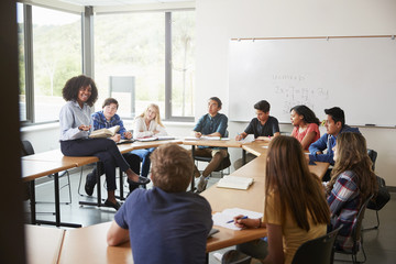 Obraz na płótnie Canvas Female High School Tutor Sitting At Table With Pupils Teaching Maths Class