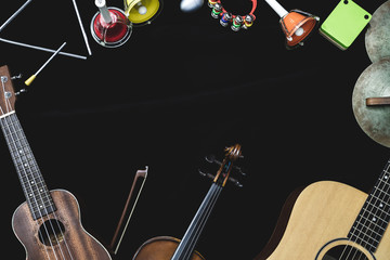Top view of violin guitar and ukulele with percussion instruments on the black background