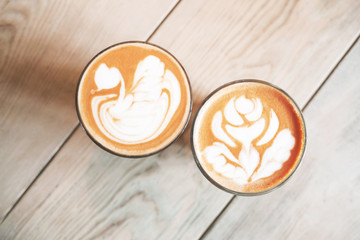 Two glasses of cappuccino with latte art on wooden table. Close up, top view.