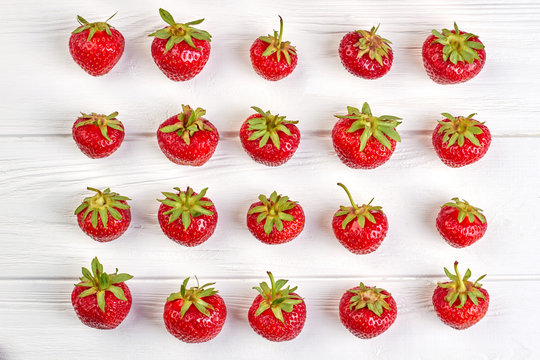 Arrangement of organic strawberries on white background. Rows of ripe juicy berries on white wooden surface. Summer fruity background.