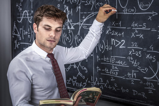 Caucasian teacher at work teaches math, classic slate blackboard with mathematical symbols. studio shot. education and study concept.