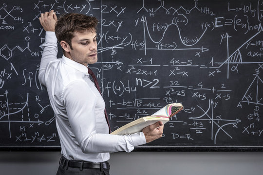 Caucasian teacher at work teaches math, classic slate blackboard with mathematical symbols. studio shot. education and study concept.