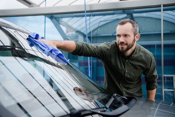 handsome man cleaning car window at car wash with rag