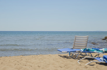 image of sun lounger and white plastic chair on the beach with sea and background
