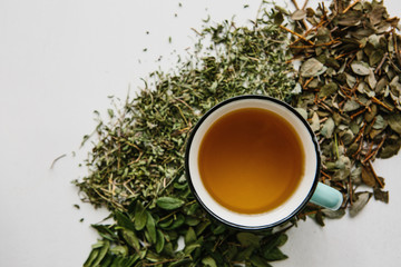 Fresh fragrant and healthy herbal tea in a glass or mug on a white wooden surface. Next to it lie various dried herbs for making tea. Healthy product
