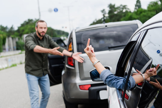 cropped image of driver showing middle finger to man on road