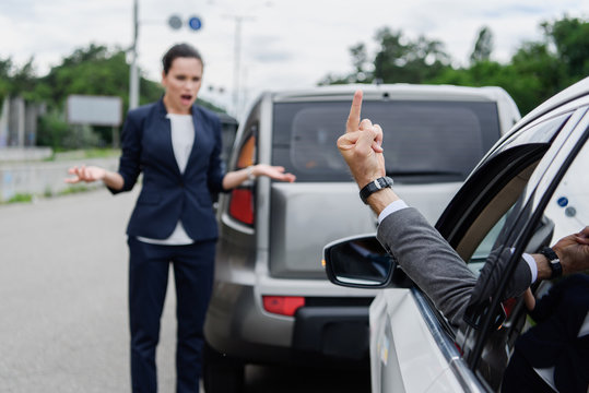 cropped image of driver showing middle finger to businesswoman on road