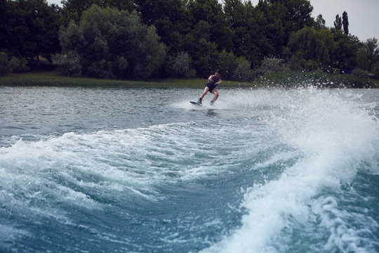 People, active lifestyle, watersports and summertime concept. Outdoor portrait of young man wakeboarding on lake, doing tricks, riding waves, using ski rope while being towed behind motor boat