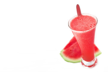 Natural cold watermelon juice against a white background next to some fruit slices. Smoothie and empty copy space for Editor's text.