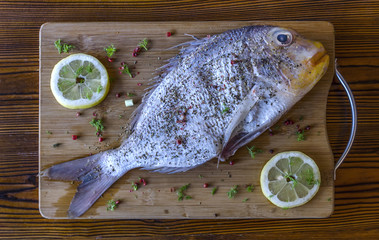 Fresh uncooked seabream fish with lemon, herbs, pepper and spices on wooden cutting board and...