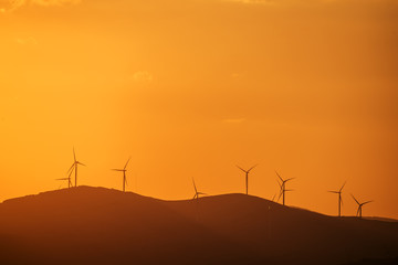 Wind power generator on a hill  at sunset, silhouettes of mountain peaks.
