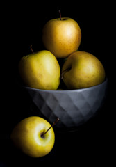 Bowl of yellow apples. On black background.