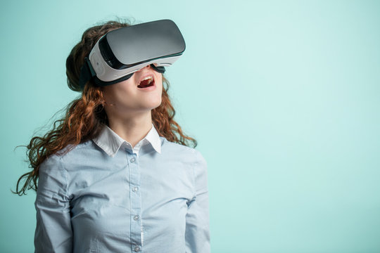 Beautiful Ginger Girl In Virtual Reality Goggles. Isolated Blue Background. Copyspace. Unimaginable Enviroment. Admire With Virtual Life.