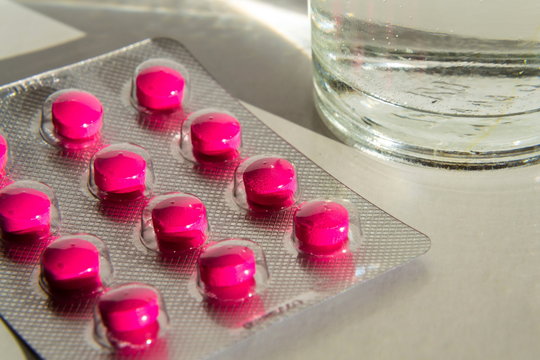 Detail of bright pink pills in medicine capsule with glass of water isolated on white background, pain migraine fever illness medicine concept