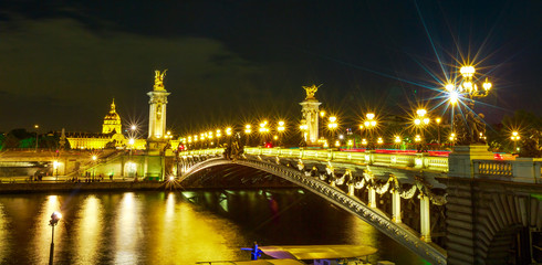 Panorama of Paris lights on in Pont Alexandre III bridge with lighted lamps. French European capital in Parisian night skyline of France. Night urban wide scene.