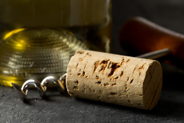 Brown natural wine cork with corkscrew and bottle of white wine on dark table
