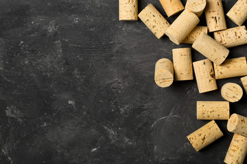 Heap of unused, new, brown natural wine corks on dark wooden board, flat lay top view