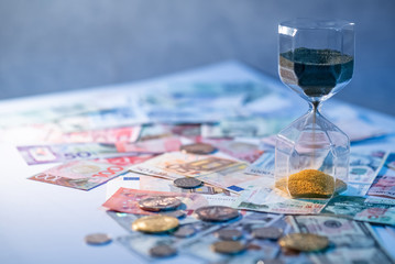 Sand running through the shape of hourglass on table with banknotes and coins of international...