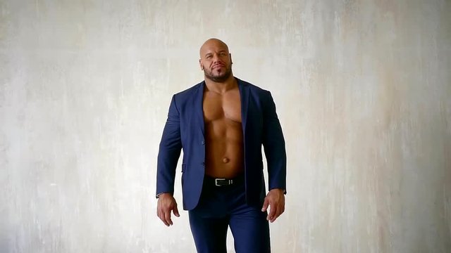 confident bodybuilder dressed in luxury blue suit with unbuttoned jacket, demonstrating naked chest