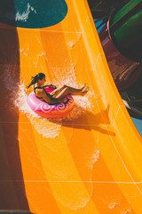 pretty young woman on the pink rubber ring having fun on the orange water slide in the aqua park. Summer Vacation. Weekend on resort