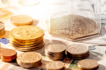 Various of international money coins and bitcoin with hourglass on banknote. Time investment with currency exchange. Worldwide cryptocurrency and digital payment concept