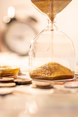 Sand running through the shape of hourglass on table with banknotes and coins of international...