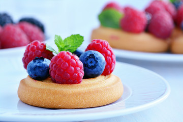 Soft sugar cookies topped with fresh forest fruits, raspberries, blackberries, blueberries on white plate