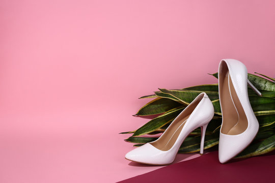  White women's leather shoes lie on a plant on a pink background