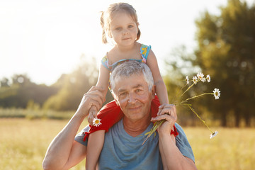 Senior wrinkled grey haired grandfather gives piggyback ride to his granddaughter, have walk in...