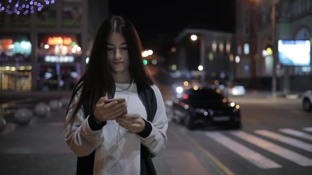 Woman walking at night city use smartphone listening to music in downtown