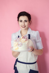 confectioner in a white apron on a pink background with a cake