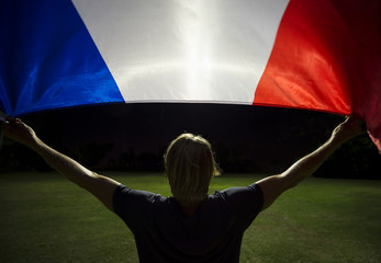 Fototapeta na wymiar Man waving french tricolor flag on grass pitch backlit by bright floodlights